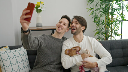Two men couple making selfie by smartphone sitting on sofa with dog at home