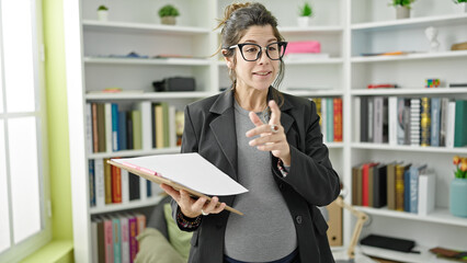 Young pregnant woman teacher holding clipboard explaining lesson at library university