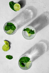 Summer refreshing cocktail Mojito with rum, mint, lime and ice in glass on a white stone background and hard light with long shadows. Virgin Mojito is a summer non-alcoholic cocktail.