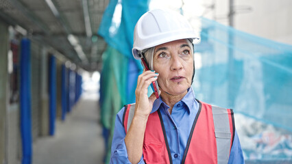 Middle age grey-haired woman builder talking on smartphone at street