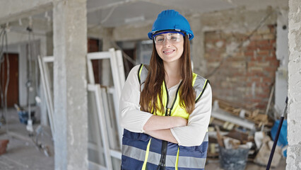 Young beautiful hispanic woman builder smiling confident standing with arms crossed gesture at construction site