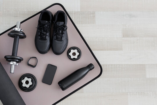 Flat lay of dumbbells, shoes, water bottle, watch and phone on sport mat