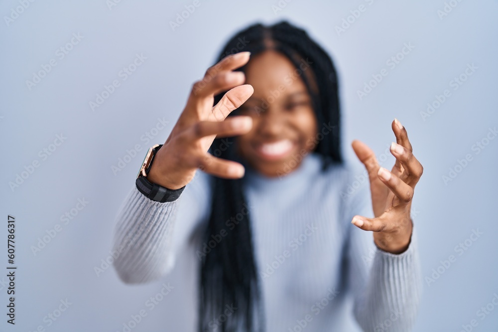 Sticker african american woman standing over blue background shouting frustrated with rage, hands trying to 