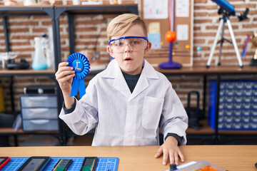 Little caucasian boy at school scientist laboratory winning first prize scared and amazed with open mouth for surprise, disbelief face