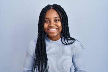 African american woman standing over blue background with hands together and crossed fingers smiling relaxed and cheerful. success and optimistic