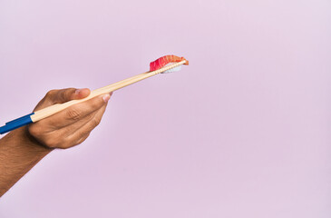  Hand of man holding tuna nigiri with chopsticks over isolated pink background