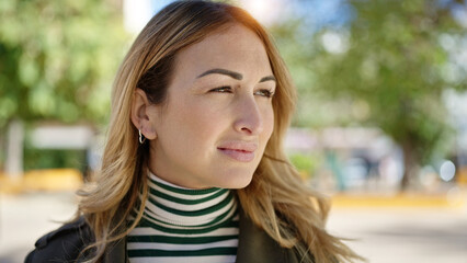 Young beautiful hispanic woman standing with serious expression looking to the side at park