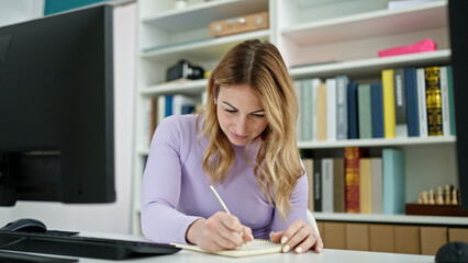 Young beautiful hispanic woman student using computer writing on notebook at library university
