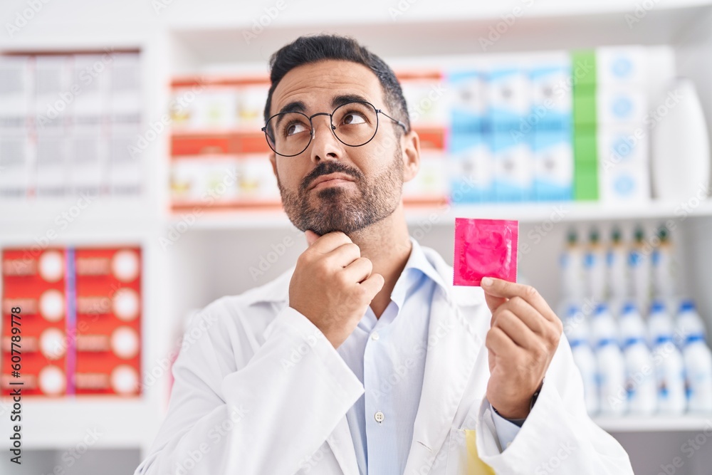 Wall mural hispanic man with beard working at pharmacy drugstore holding condom serious face thinking about que