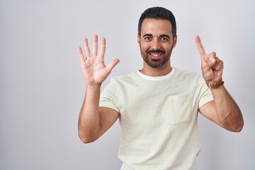 Fototapeta premium Hispanic man with beard standing over isolated background showing and pointing up with fingers number six while smiling confident and happy.