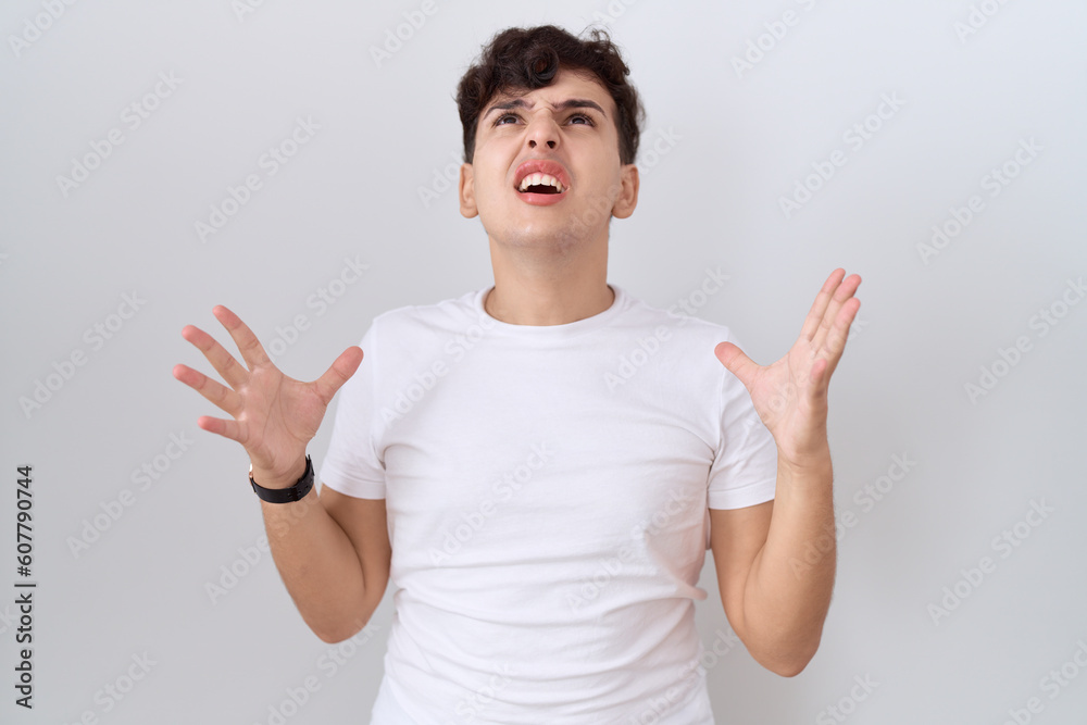 Poster young non binary man wearing casual white t shirt crazy and mad shouting and yelling with aggressive