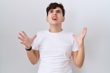 Young non binary man wearing casual white t shirt crazy and mad shouting and yelling with aggressive expression and arms raised. frustration concept.