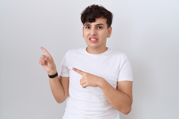 Young non binary man wearing casual white t shirt pointing aside worried and nervous with both hands, concerned and surprised expression