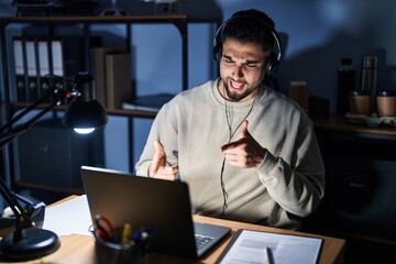 Young handsome man working using computer laptop at night pointing fingers to camera with happy and funny face. good energy and vibes.