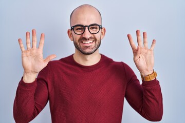 Naklejka premium Young bald man with beard standing over white background wearing glasses showing and pointing up with fingers number nine while smiling confident and happy.