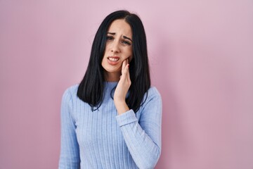 Fototapeta premium Hispanic woman standing over pink background touching mouth with hand with painful expression because of toothache or dental illness on teeth. dentist
