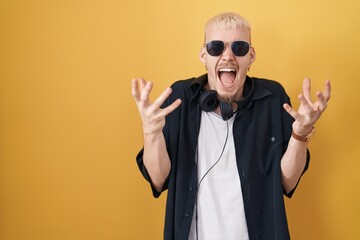 Young caucasian man wearing sunglasses standing over yellow background celebrating mad and crazy for success with arms raised and closed eyes screaming excited. winner concept