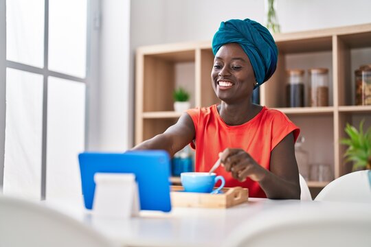 Young african american woman having breakfast watching video on touchpad at home