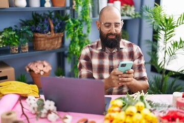 Young bald man florist using smartphone and laptop at flower shop