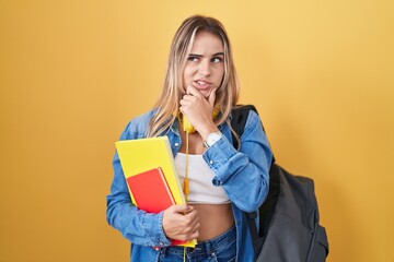 Young blonde woman wearing student backpack and holding books thinking worried about a question, concerned and nervous with hand on chin