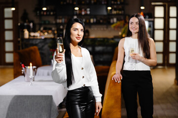 Beautiful young couple of women with glasses of champagne are celebrating in luxury restaurant
