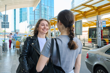 Two young female students at a bus stop in a modern city