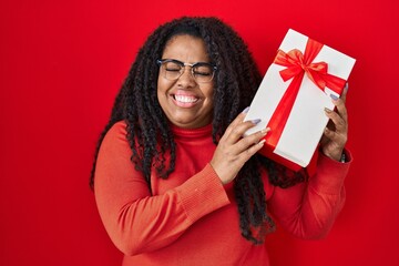 Plus size hispanic woman holding gift smiling with a happy and cool smile on face. showing teeth.
