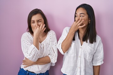 Hispanic mother and daughter together smelling something stinky and disgusting, intolerable smell,...