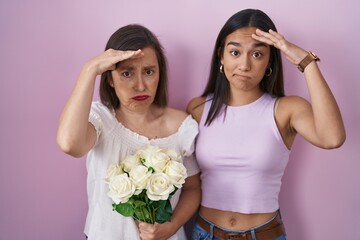 Hispanic mother and daughter holding bouquet of white flowers worried and stressed about a problem with hand on forehead, nervous and anxious for crisis