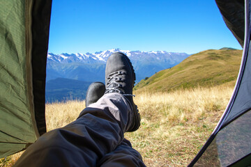 leg tourist in boots out of the tent with mountains in the background - obrazy, fototapety, plakaty