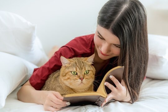 Young Asian woman reading book with her cat at home