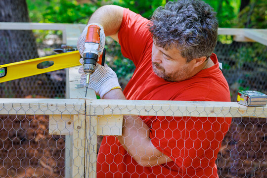 Worker uses screwdriver to wooden domestic chicken coop on farm that contains metal grid