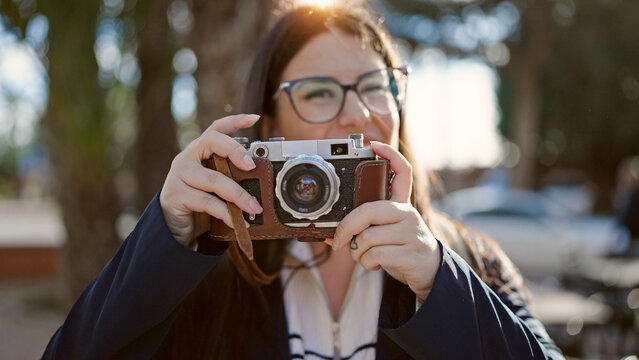 Young hispanic woman tourist wearing backpack taking pictures with camera at street