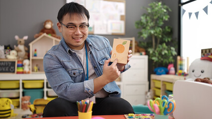 Fototapeta premium Young chinese man preschool teacher having vocabulary lesson at kindergarten
