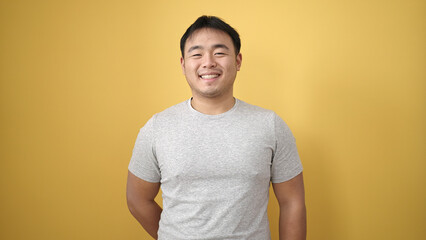 Young chinese man smiling confident standing over isolated yellow background