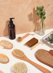 A pattern of ecological wooden massage and shower brushes different shape with natural bristles on a white table. Natural soap on a soap dish. Dispenser with shower gel.