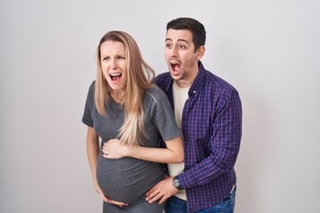 Young couple expecting a baby standing over white background angry and mad screaming frustrated and furious, shouting with anger. rage and aggressive concept.
