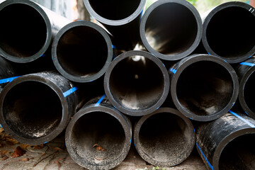 Pile of black HDPE pipes prepared for water transportation. Many plastic irrigation pipes made of high-density polyethylene