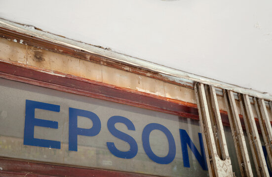 Ho Chi Minh City, Vietnam - May 22, 2023: Blue Epson logo in a window of a printer service center. Dirty old advertisement of a Japanese electronics manufacturer