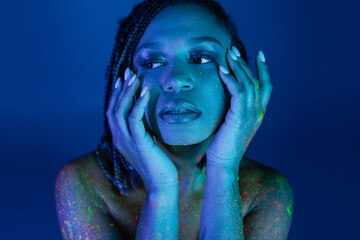 tempting african american woman with dreadlocks holding hands near face while posing in colorful...