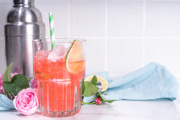 Rose flower lemonade, refreshing summer drink with crushed ice, rose petals and syrup, lime slices. Light rose cocktail, sour rose wine