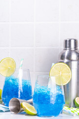 Iced blue curacao cocktail, drunken mermaid alcohol cocktail drink with lime slice garnish and crushed ice, on white kitchen background copy space