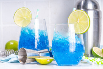 Iced blue curacao cocktail, drunken mermaid alcohol cocktail drink with lime slice garnish and crushed ice, on white kitchen background copy space