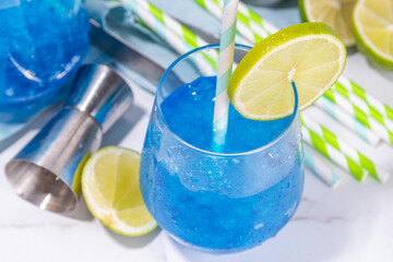 Iced blue curacao cocktail, drunken mermaid alcohol cocktail drink with lime slice garnish and crushed ice, on white kitchen background copy space