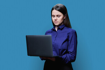 Portrait of young woman with laptop on blue background