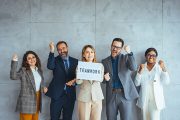 Fototapeta premium Portrait of multi ethnic successful business team looking at camera in the office and team leader holding sign ''teamwork'' in hands. Business men and women managers team holding big teamwork banner.