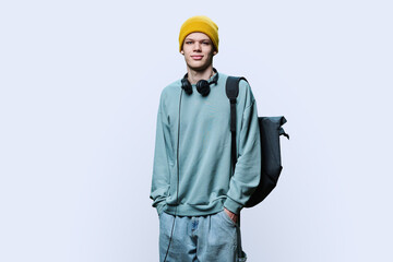 Young male in yellow cap sweatshirt with headphones backpack on white background