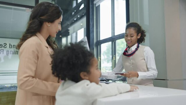American african women airline ground staff worker giving boarding pass or ticket to passenger woman mother and little daughter at airport check in counter. Family travelling concept
