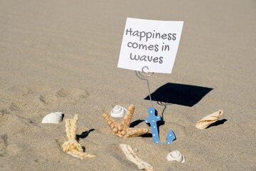 HAPPINESS COMES IN WAVES text on paper greeting card in anchor paper holder and starfish seashell summer vacation decor. Sandy beach sun coast. Holiday concept postcard. Getting away Travel Business