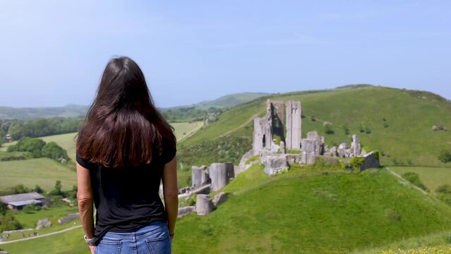 A tourist woman looks at the ruins of Corfe Castle, Dorset, England, during a sunny spring day